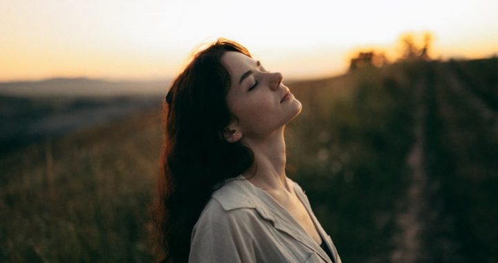 A serene woman with head tilted back, savoring the warm sunset in a field.
